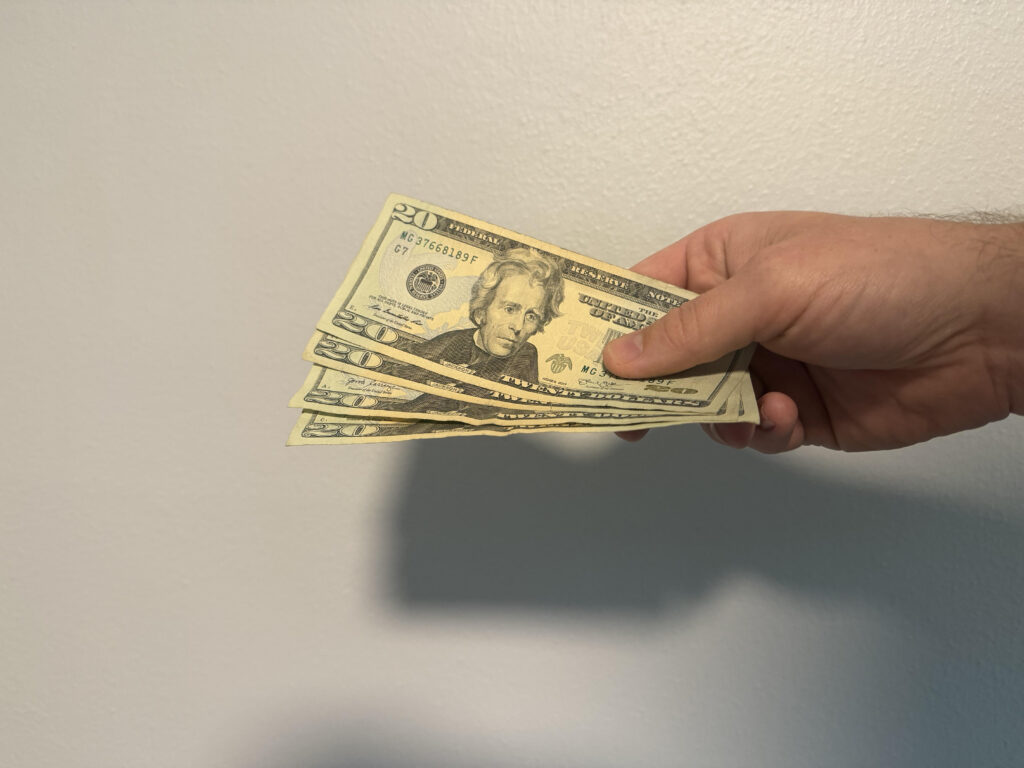Four $20 Bills are offered by a hand to show the return of money for a purchase.